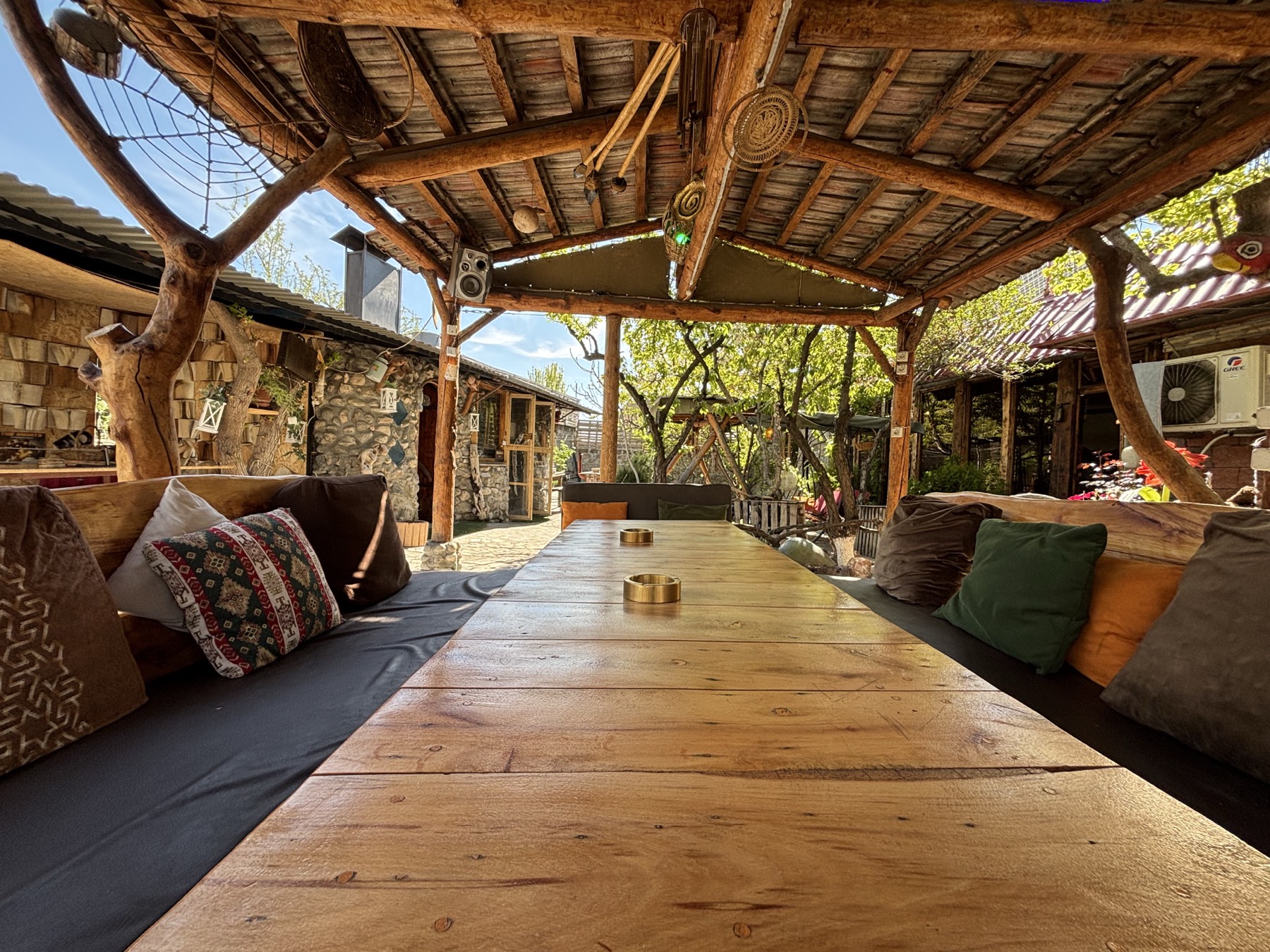 The long gazebo table close up, with kilim cushions along both benches and brass ashtrays on the boards